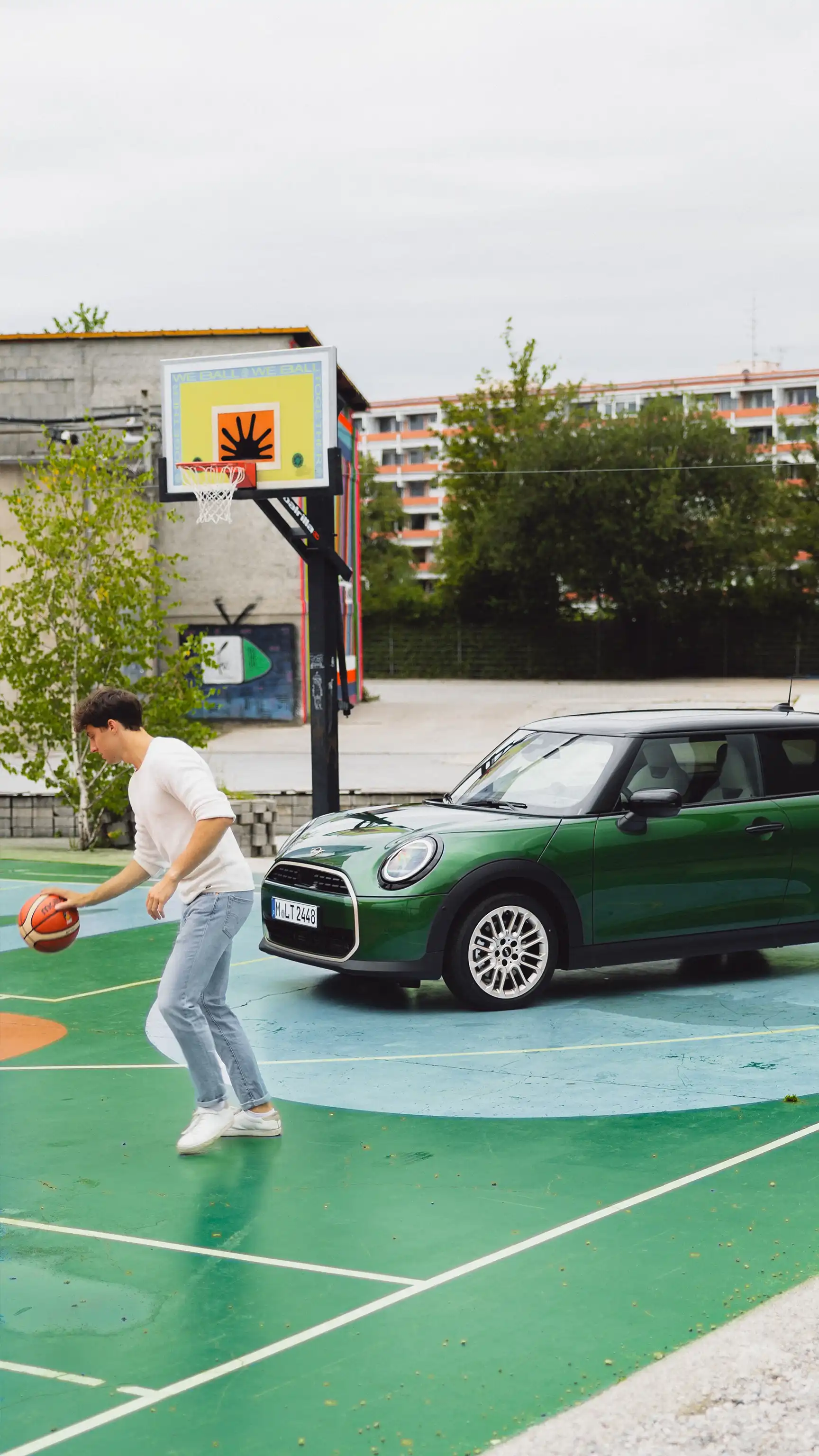 Personne dribblant un ballon de basket sur un terrain extérieur à côté d’un MINI Cooper.
