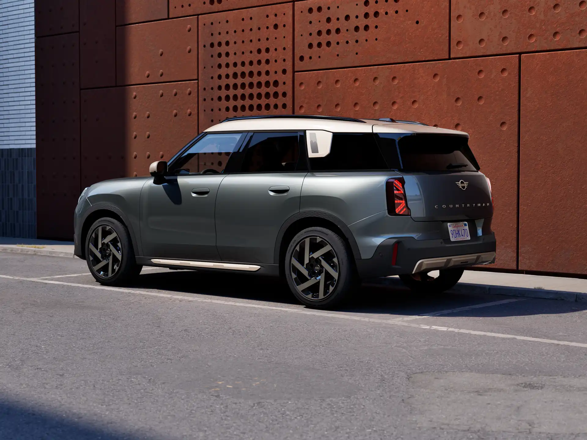 Vue arrière trois quarts d’un MINI Countryman stationné à côté d’un mur couleur rouille.