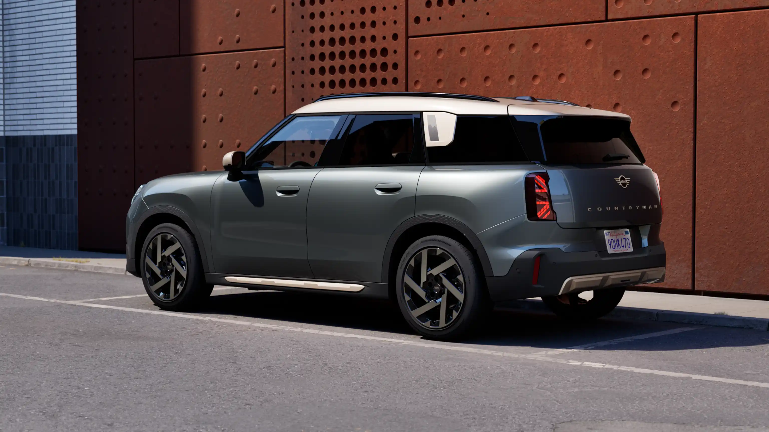 Vue arrière trois quarts d’un MINI Countryman stationné à côté d’un mur couleur rouille.