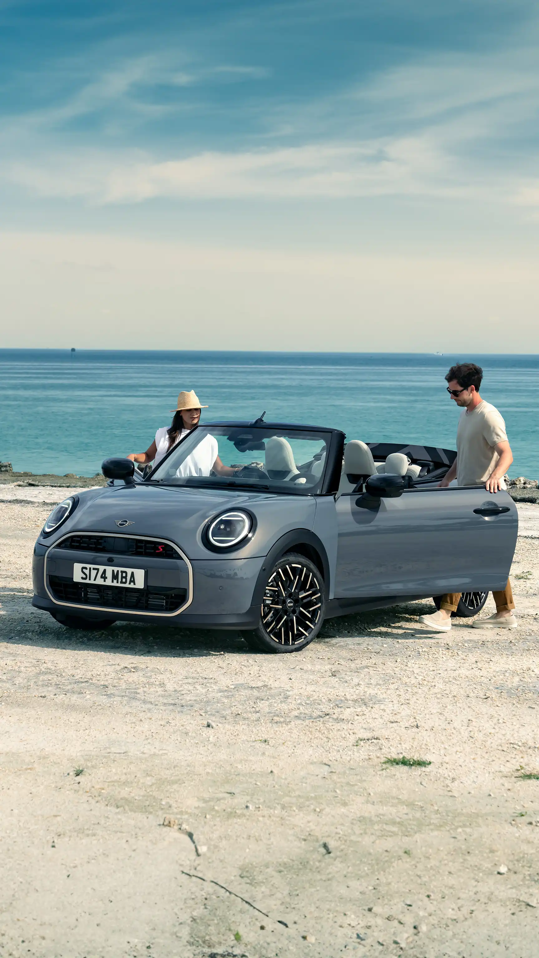 MINI Cabriolet en Melting Silver Metallic stationné en bord de plage tandis que deux personnes se tiennent à côté.